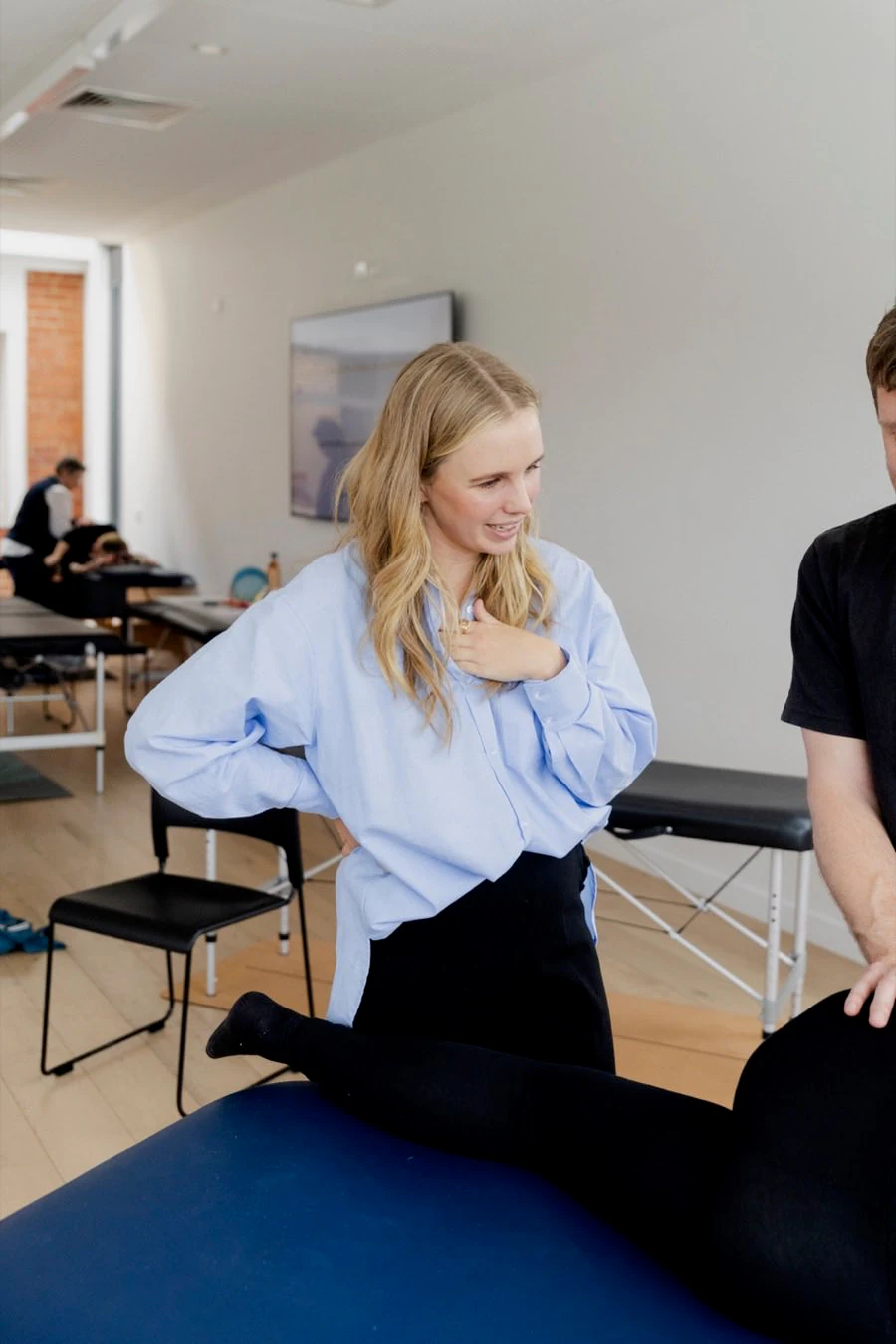 Lani Merrick teaching a birth preparation class, demonstrating a position with her hands on her hips while a participant works through it on a table beside her.