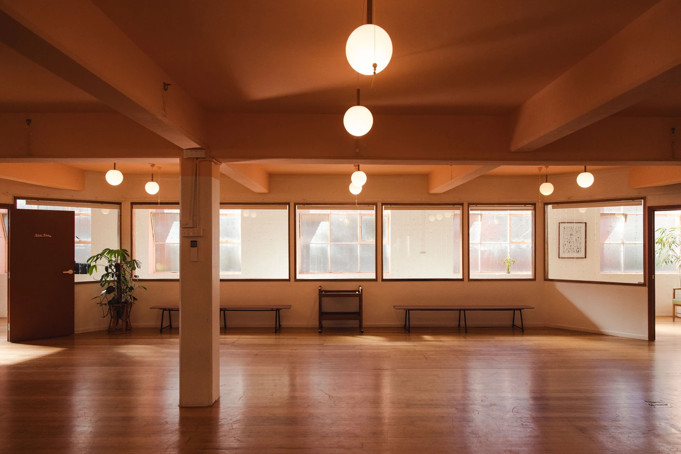 The same room from the window side: a row of tall windows with low benches beneath them, a structural pillar mid-floor and an open door at one end.